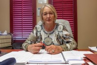 A photo of a woman seated at her desk. Paperwork is in front of her and she is holding a pen in her hands.