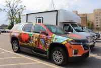 A colorfully decorated SUV is parked beside a white truck.
