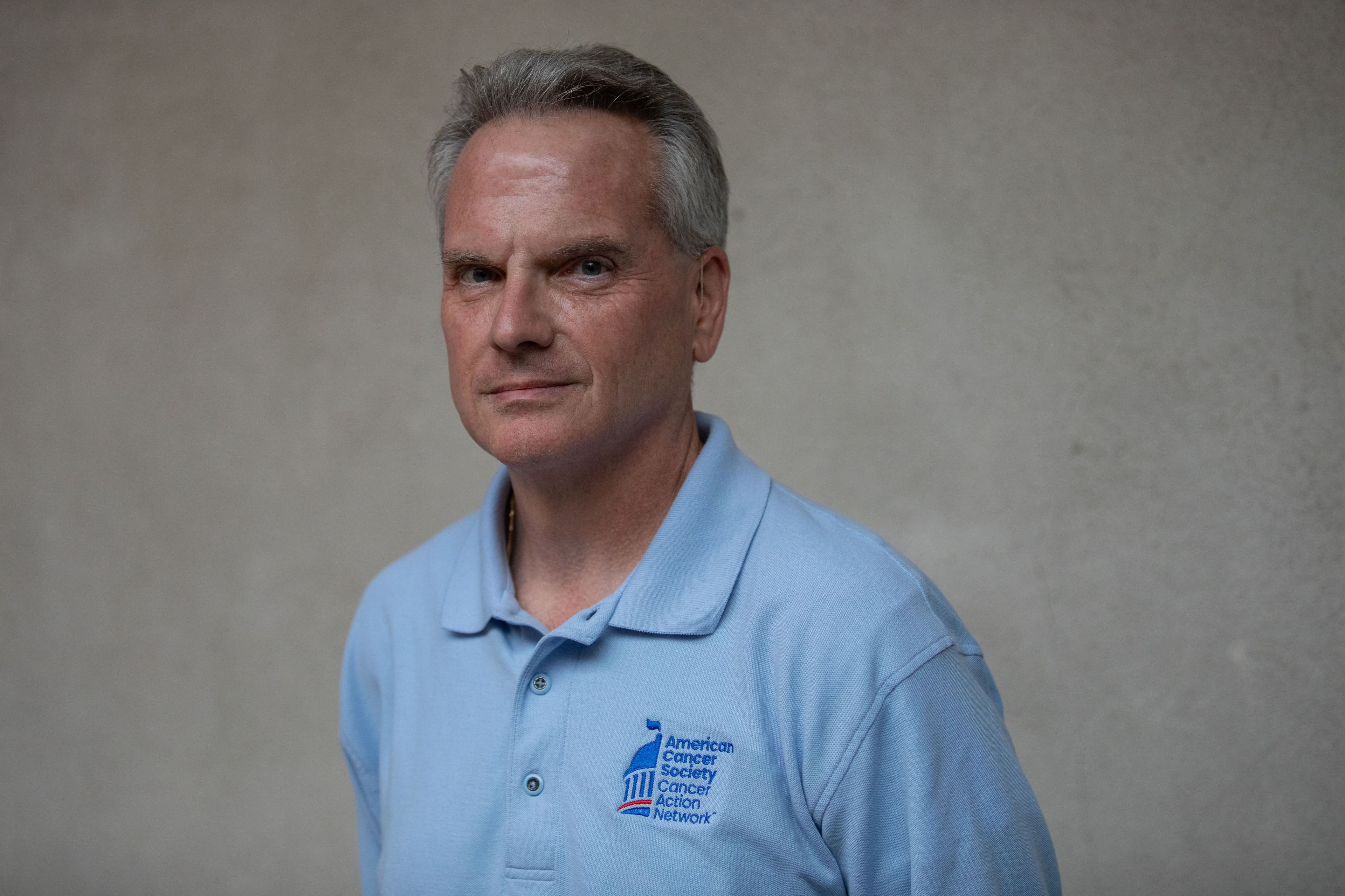 A portrait of an older man wearing a blue shirt against a grey background.