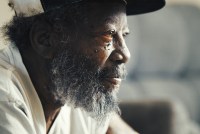 A man with a beard wearing a baseball cap and a white shirt looks toward the right side of the frame