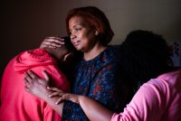 A mother embraces her two children, whose faces are hidden from view.
