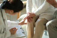 A young doctor checks her elderly patient's knee.