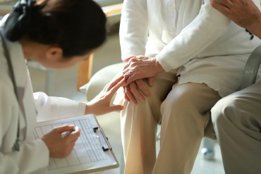 A young doctor checks her elderly patient's knee.