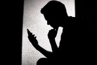 A photo of a young man in silhouette. He is looking at his phone.
