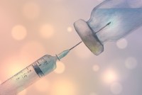 An illustration in watercolor of a syringe and vaccine vial against a soft background of dotted light.
