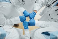 Five doctors in doctors in lab coats and blue gloves fist-bump.