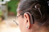 A closeup shot of the side of a woman with a cochlear implant who is also wearing reading glasses.