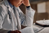An unidentifiable female doctor works at a desk deep in thought.