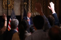 Donald Trump is pictured from afar. The raised hands of reporters are seen in the foreground.