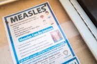 A photo of a flyer that reads, "Measles: Measles symptoms include high fever, cough, runny nose, red and watery eyes, rash breakout 3-5 days after symptoms begin. Measles can be serious. 1 out of 5 people who get measles will be hospitalized. One person can make 12 people sick. If someone in your family has measles, please try to stay away from other people."
