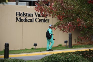 An unidentifiable person in scrubs walks beside a tan wall with a sign reading "Holston Valley Medical Center" on it.