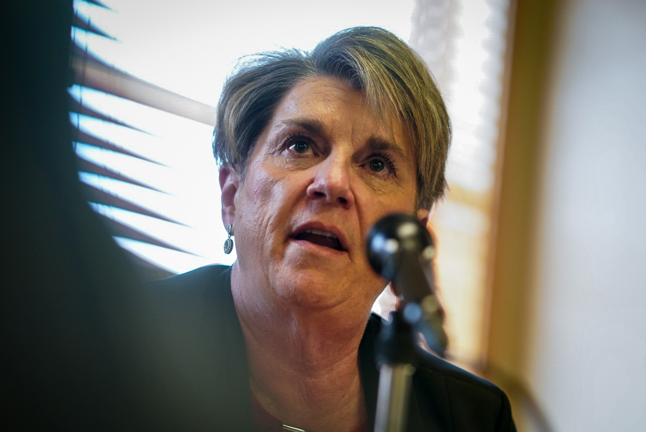 A middle aged woman with short-cut blonde hair speaks into a microphone.