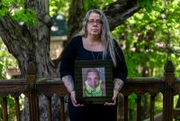 A portrait of a mother standing outside, holding a picture of her late son.