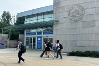 A photo of the NIH campus on a partly-cloudy day. A few pedestrians walk past an entrance to the building.