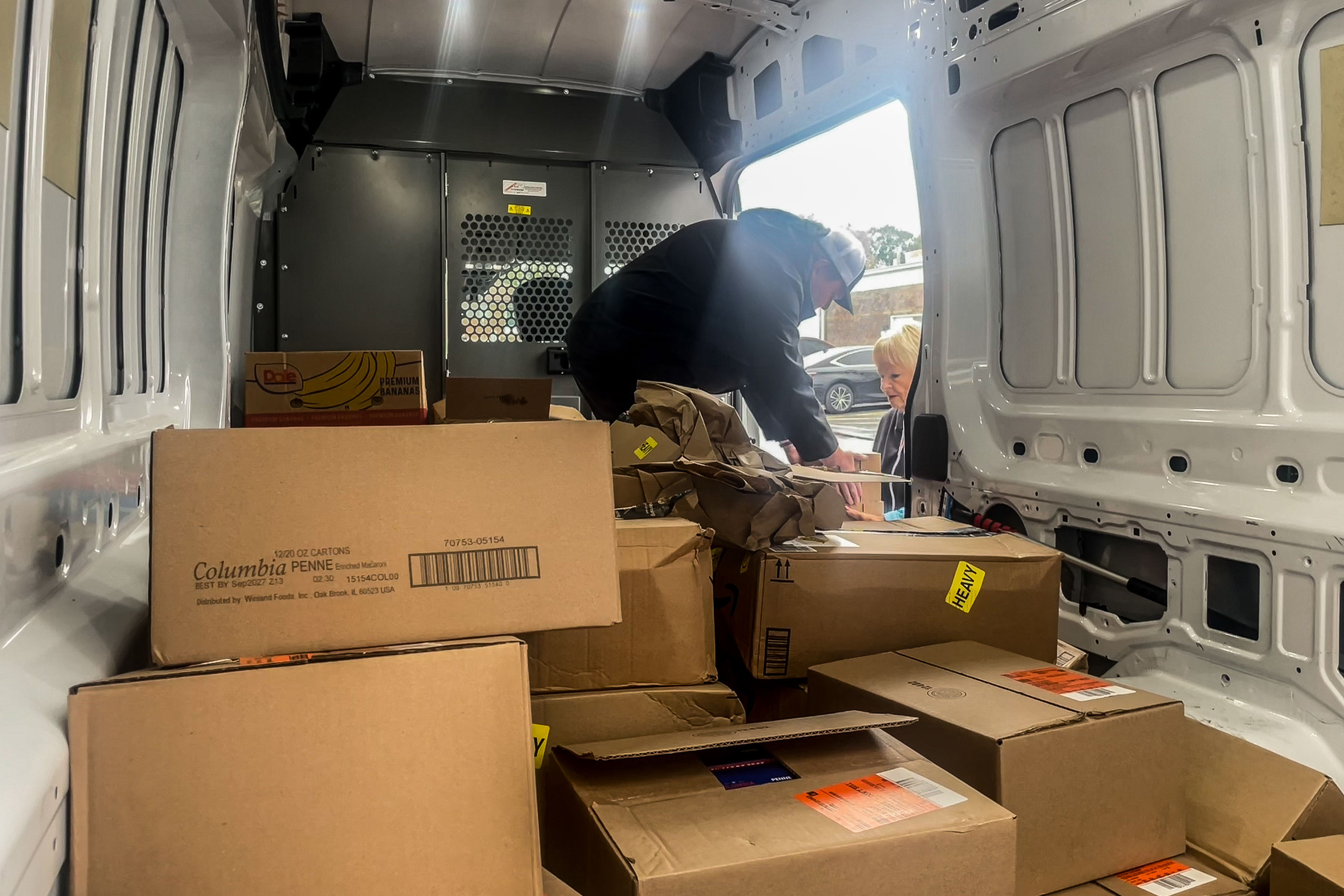 A man unpacks boxes from the back of a white van