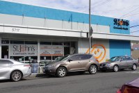 A photo of a health clinic's exterior. Cars are parked on the street in front of it.