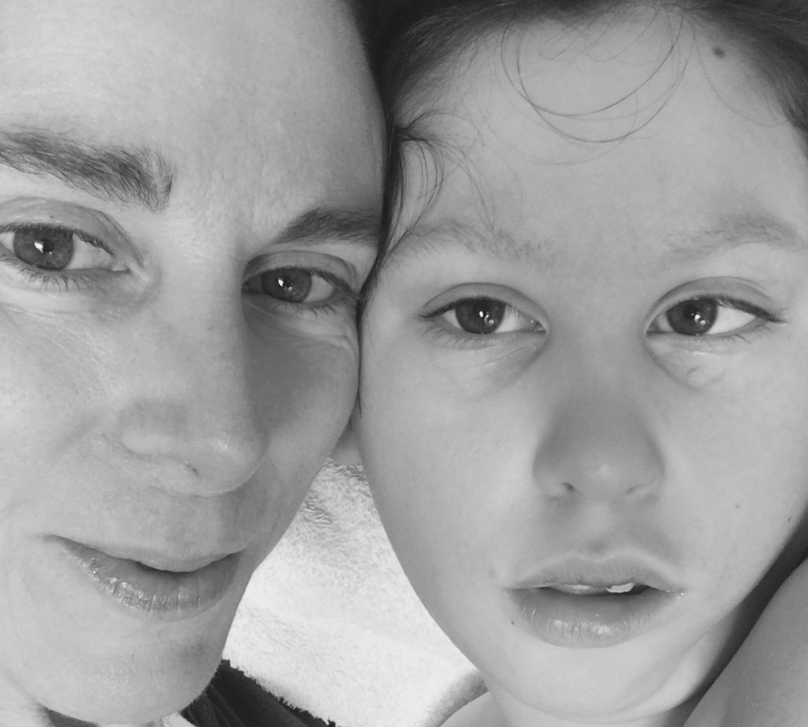 A close up of a woman and young boy, the sides of their faces touching