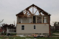 A photo of a house severely damaged by a tornado. The upper half's walls have blown away, leaving just the roof frame behind.