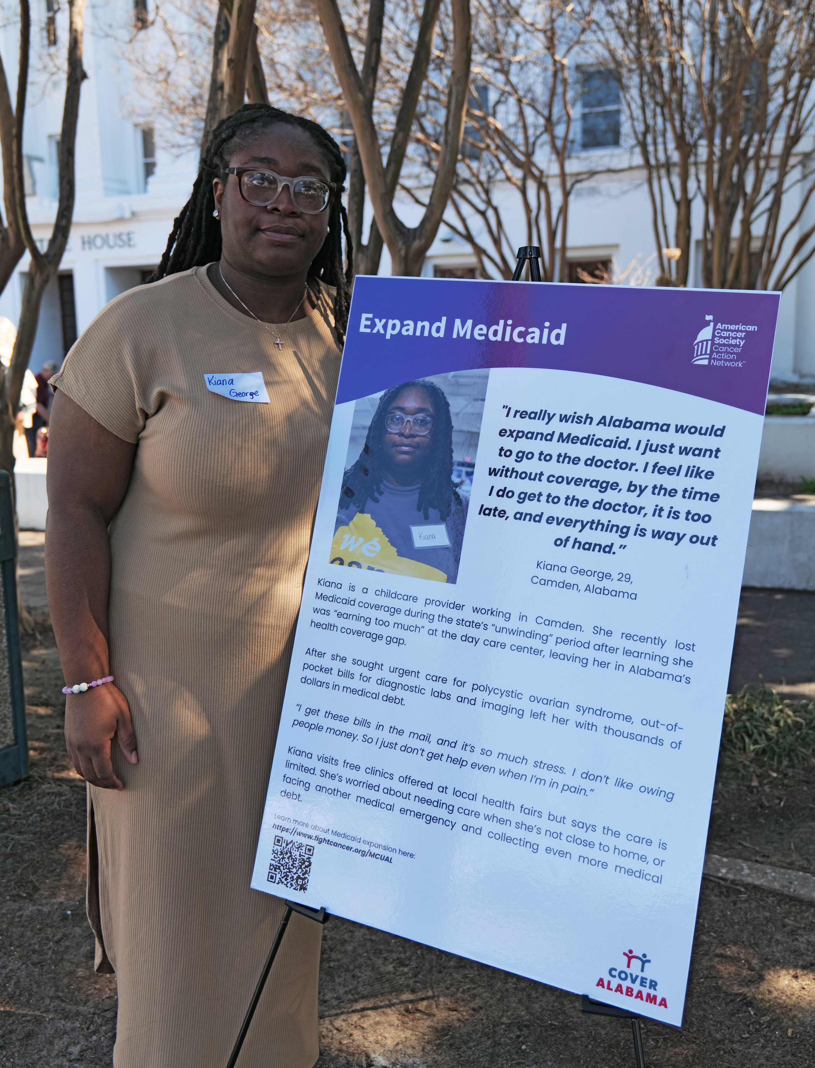 A photo of Kiana George standing for a photo outdoors. She stands next to a sign that reads, "Expand Medicaid," followed by a quote describing her opinions on the issue and an explanation of her story.