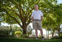 A photo of a man standing outside under a shaded canopy of trees.