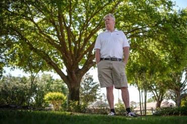 A photo of a man standing outside under a shaded canopy of trees.